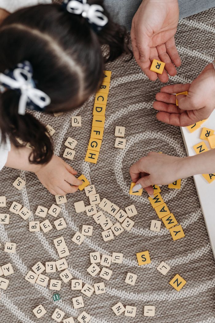 about-us-02 Family playing a word game with tiles on a patterned carpet, showcasing togetherness and learning.